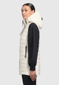 Weste aus Puffer-Material in Creme mit abnehmbarer Kapuze, seitlichen Taschen und schwarzen langen Ärmeln. Strukturiertes, gestepptes Design mit einer schlanken Form.