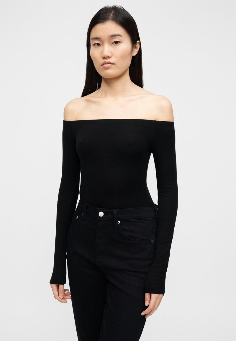 Body noir à manches longues, épaules dénudées, en tissu lisse et extensible, associé à un jean noir taille haute avec fermeture à boutons.