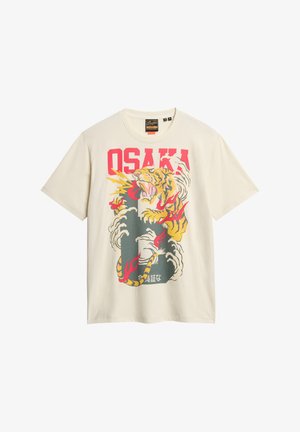 Crème-kleurige t-shirt met een kleurrafische afbeelding van een tijger omringd door wolken en het woord "OSAKA" in dikke rode letters. Korte mouwen.