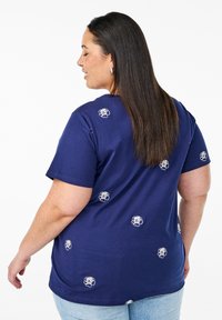 Námořnická modrá tričko vyrobené z bavlny, s bílou květinovou výšivkou rozptýlenou po zadní části. Krátké rukávy, volný střih, kulatý výstřih.