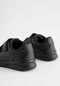 Scarpe da ginnastica nere con tomaia in pelle liscia, cintura a strappo, colletto imbottito e suola in gomma texturizzata per grip e comfort.