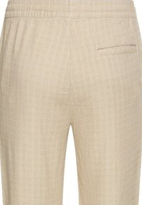 Beige Hose aus strukturiertem Stoff, mit elastischem Bund und einer hinteren Tasche. Dezentes Karomuster im gesamten Design.