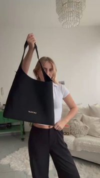 Black fabric tote bag with shoulder straps, features gold "Valentino" logo on front, smooth texture, large open shape.