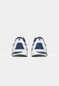 Adidași albi și bleumarin cu un superior din plasă texturată, talpă intermediară amortizată, călcâi structurat și talpă din cauciuc cu modele de profil.