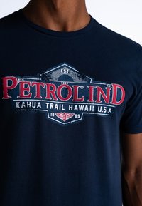 Námořnická modrá bavlněná tričko s vintage-style grafikou s textem "Petrol Ind" v červené barvě a "Kahua Trail Hawaii U.S.A." Crew neck design.