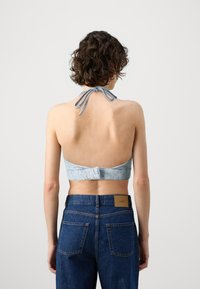 Bralette in denim di un blu chiaro con collo halter, caratterizzato da una vestibilità aderente sul retro e una chiusura con gancetto, abbinato a jeans a vita alta di un blu scuro.