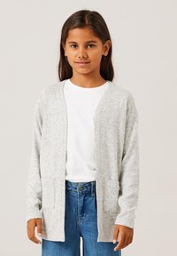 Cardigan grigio con texture, aperto sul davanti, due tasche frontali, abbinato a una camicia bianca e jeans blu. Il tessuto appare morbido e casual.
