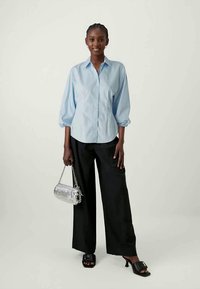 Φωτεινό μπλε πουκάμισο με φουσκωτά μανίκια, συνδυασμένο με μαύρους παντελόνες φαρδιές. Τα αξεσουάρ περιλαμβάνουν μια ασημένια τσάντα και μαύρες open-toe γόβες.