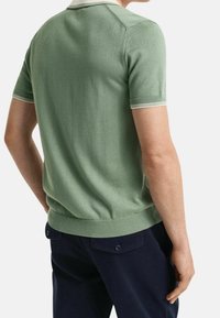 Polo vert en maille avec manches courtes, doté d'un col et de poignets rayés blancs. Texture lisse, coupe ajustée, ourlet côtelé.