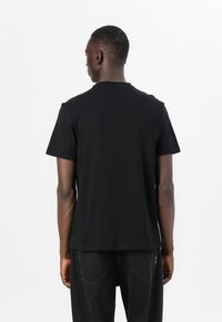 Zwarte katoenen t-shirt met korte mouwen, voorzien van een ronden hals en een gladde, egale textuur, gedragen met donkere jeans.