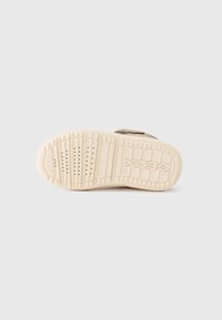 Beige sneaker sula med texturerad gummi, med ett möntrat däck för grepp och präglat logotyp. Detalj med kardborreband på ovansidan.