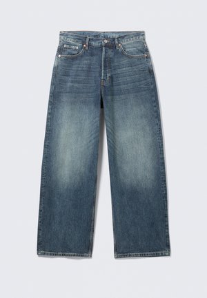 Jeans azules de pierna ancha con muslos delanteros descoloridos, cinco bolsillos, cierre de botones y presillas para cinturón, extendidos sobre un fondo claro.