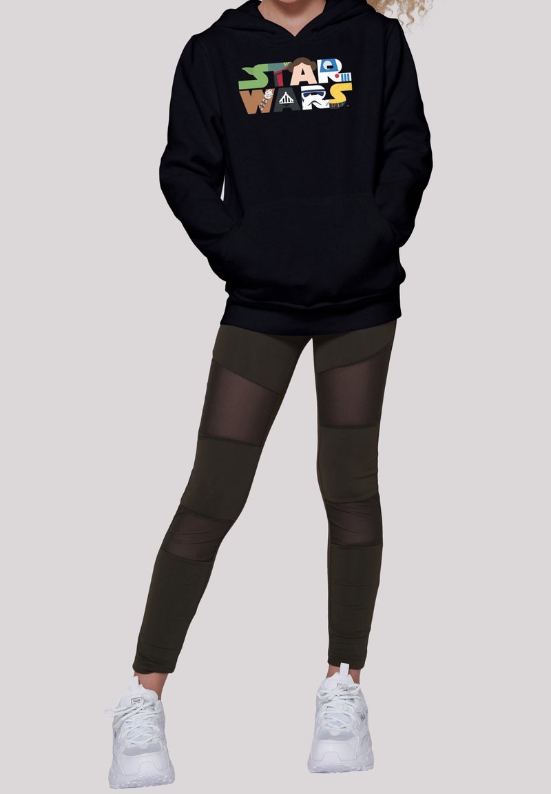 Sudadera negra con gráfico de "Star Wars" en colores vibrantes. Leggings verde oliva con paneles de malla y zapatillas blancas. Diseño simple y deportivo.