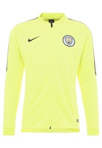 Nike Manchester City jacket in bright yellow, featuring a full zip, high collar, and team logo on the chest. Textured sides with black accents.