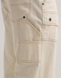 Μπεζ cargo παντελόνια με πολλαπλές τσέπες, ενισχυμένα ράμματα, πράσινα μεταλλικά στοιχεία και μια μικρή λεπτομέρεια λογότυπου στο πίσω μέρος.