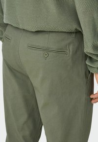 Pantalons vert olive avec une texture lisse, dotés de deux poches arrière avec des fermetures à bouton et de subtils détails de couture.