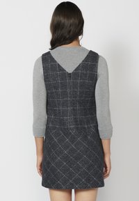 Navy blue plaid dress with a V-shaped back, crafted from textured fabric, paired with a gray long-sleeve top. Features a fitted silhouette.