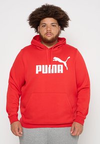 Sudadera roja con capucha, que presenta un gran logo blanco de "PUM" y un gráfico de un puma saltando en la parte frontal. El material parece suave y cuenta con un bolsillo frontal.