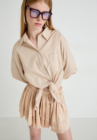 Overhemd met knopen in een lichtbeige ruitenpatroon, knoop in de taille; gecombineerd met een gestructureerde, gelaagde beige rok.
