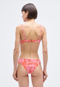 Pink floral bikini set featuring a patterned top with adjustable straps and a matching low-rise bottom, made of smooth, stretchable fabric.