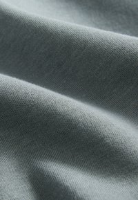 Hellgrauer Baumwollstoff mit glatter Textur, leicht gekräuselt und feinem Strickmuster, das Weichheit und Fall betont.