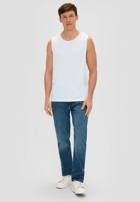 T-shirt sans manches blanche avec un col rond, associé à un jean bleu clair et des baskets blanches. Design simple, coupe décontractée et couleurs unies.