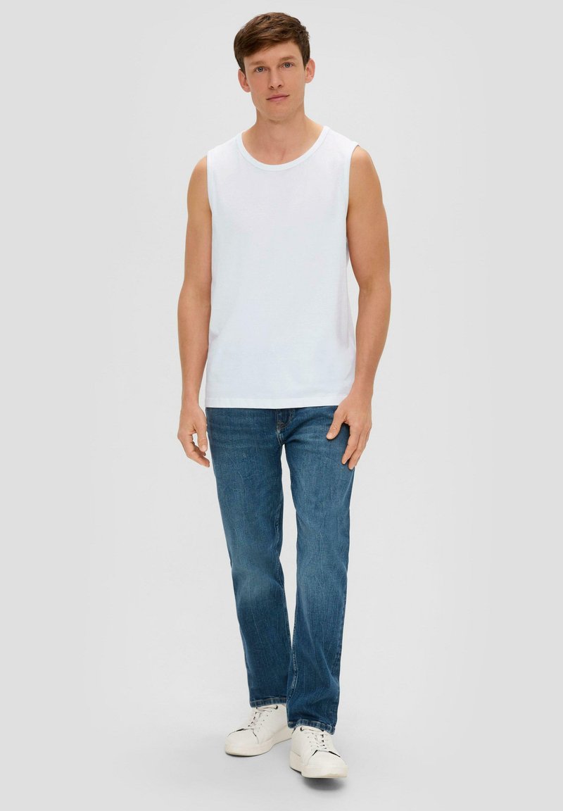T-shirt sans manches blanche avec un col rond, associé à un jean bleu clair et des baskets blanches. Design simple, coupe décontractée et couleurs unies.