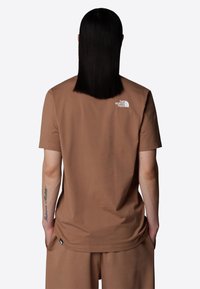 Korte broek bruine t-shirt van katoen, met een witte logo op de bovenrug en een label aan de zijkant bij de zoom.