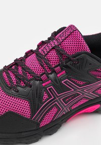 Chaussure de sport noire et rose avec une tige en mesh, des lacets texturés et un logo bien visible. Dotée d'une semelle en caoutchouc durable et d'un design léger.