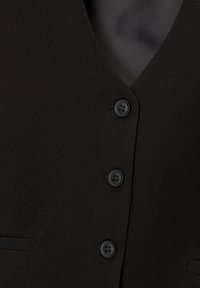 Gros plan d'un blazer noir avec trois boutons noirs et un col cranté sur un fond en tissu lisse.