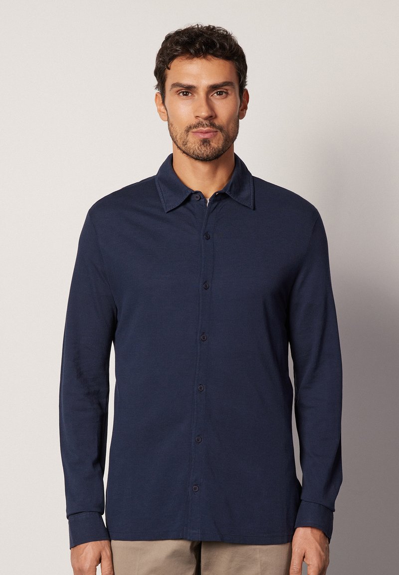 Chemise à manches longues bleu marine, en tissu doux, avec un col classique et un devant à boutonnière avec des boutons assortis et une coupe décontractée.