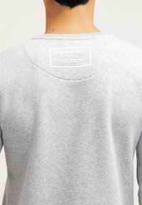 Felpa grigia con scollo rotondo e tessuto texturizzato. Presenta un'etichetta bianca sul retro con il testo "CRIMINAL DAMAGE - LONDON."