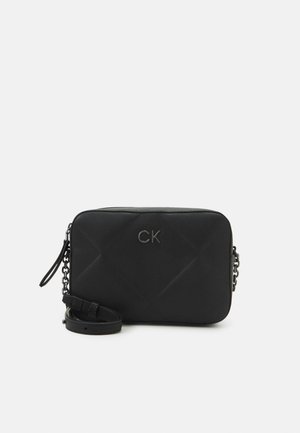 Sac bandoulière rectangulaire noir avec texture matelassée, logo métallique CK et bandoulière en cuir réglable avec des maillons de chaîne.