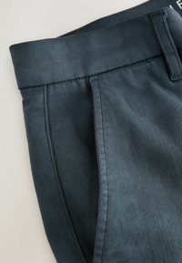 Nahaufnahme von dunkelblauen maßgeschneiderten Hosen, die den Gürtelschlaufe, den Bund und die Seitenasche mit sichtbaren Nähdetails zeigen.