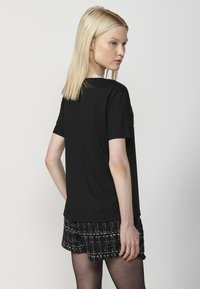 Camiseta negra de manga corta hecha de un suave tejido de algodón, con un corte ligeramente holgado. Llevada con pantalones cortos negros texturizados. Vista trasera.