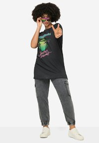 Sort grafisk t-shirt med "Electric Dreams" tryk, parret med grå cargo bukser og hvide sneakers. Model iført farverige solbriller og posering.