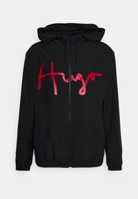 Black hooded jacket with a zip closure, elastic cuffs, and a red gradient "Hugo" logo on the front. Made from lightweight material.