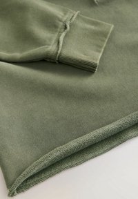 Olijfgroene sweatshirt met ribgebreide boorden en zoom, voorzien van een zachte, gladde textuur en zichtbare naaddetails langs de randen.