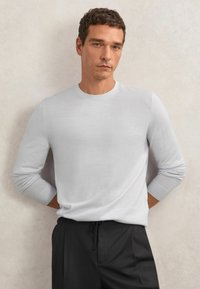 Jasnoszary sweter z długim rękawem z prążkowanym okrągłym dekoltem i mankietami, wykonany z miękkiego materiału, w zestawieniu z ciemnymi spodniami. Prosty i elegancki design.