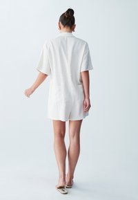 Svetlo obarvan romper z kratkimi rokavi, ovratnikom in dvema zadnjima žepoma. Narejen iz teksturirane tkanine, zasnovan za vsakodnevno nošenje.