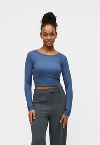 Μπλε cropped τοπ με μακριά μανίκια από ριμπ ύφασμα και στρογγυλή λαιμόκοψη, σε συνδυασμό με ψηλόμεσα γκρι παντελόνια με λεία υφή.