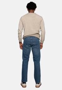 Suéter beige y jeans de mezclilla azul. Los jeans tienen un corte recto, cinco bolsillos y un ligero desgaste. Los zapatos son oscuros con una suela clara.