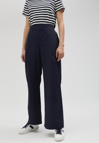 Navy high-waisted wide-leg trousers made of smooth fabric, paired with a striped navy and white t-shirt and white sneakers.