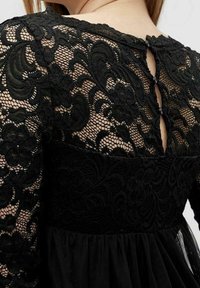 Svart spetsklänning med ett genomskinligt blommönster på bodice, med en solid svart midja och en nyckelhålsdetalj bak. Texturerad tyg.