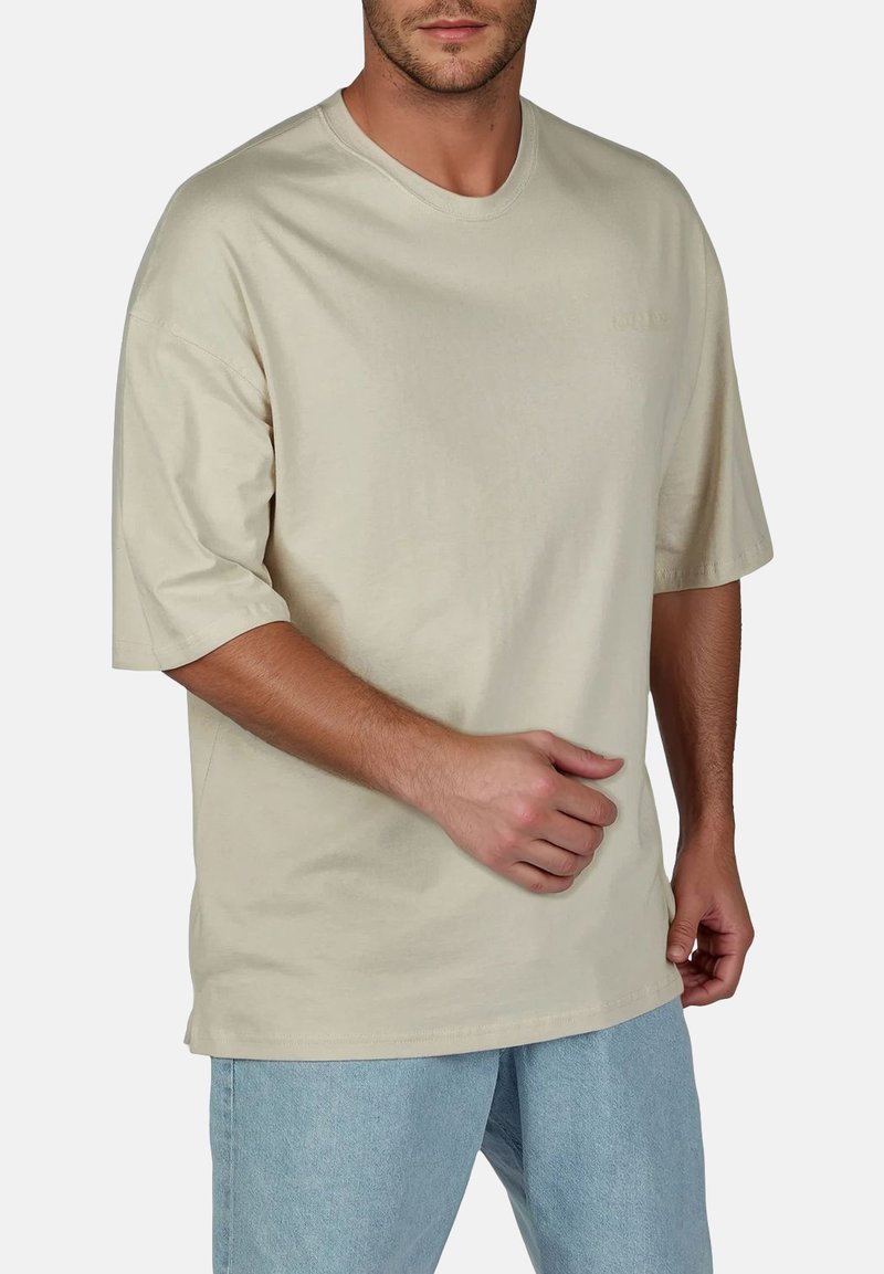 Beige katoenen t-shirt met een ronde hals, korte mouwen en een relaxed fit. Heeft een minimale branding op de voorkant.