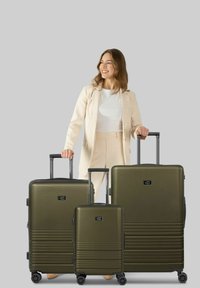 Tre valigie rigide di colore verde oliva di diverse dimensioni con superfici testurizzate, maniglie estraibili e quattro ruote ciascuna per la mobilità.