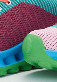 Ténis coloridos com um cabedal texturizado em bordô, detalhes em rosa e verde, sola azul e atacadores listrados em turquesa.