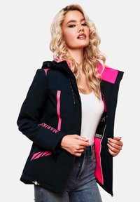 Woman with long curly blonde hair wearing a black and pink hooded jacket over a white top and blue jeans, holding the jacket open.