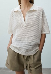 White perforated shirt with a deep V-neck and contrasting collar, paired with olive green shorts featuring a drawstring waist.