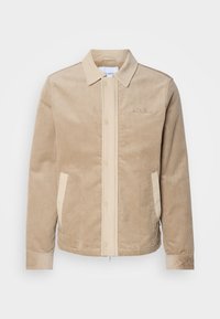 Veste en velours beige avec col, boutons-pression à l'avant, poches latérales et logo brodé discret sur la poitrine.